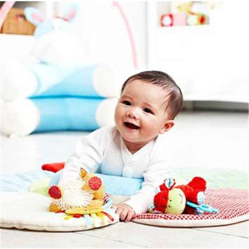 Happy baby playing on an inflatable fabric crawling play mat with colorful toys in a cozy indoor setting.