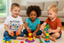 Three children playing with colorful building blocks in a living room.