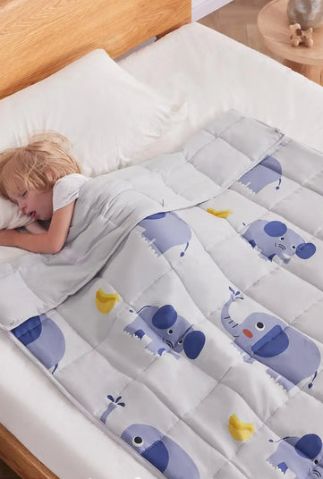 Kid peacefully sleeping under Anfie sensory weighted blanket with elephant designs on a bed.