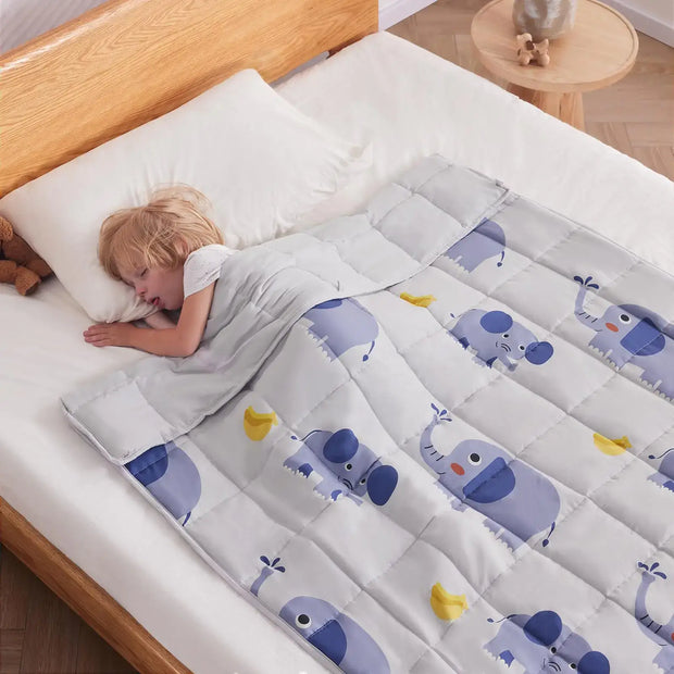 Kid peacefully sleeping under Anfie sensory weighted blanket with elephant designs on a bed.
